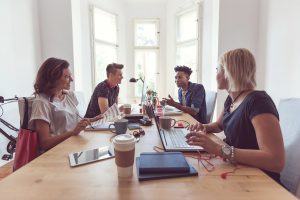 Multi ethnic group of cool young people sitting at the table and working together, using laptop, computer, discussing.